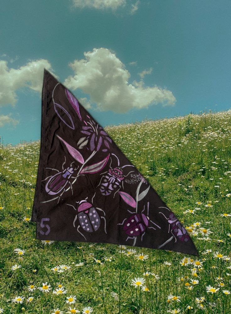Beetle Bandana No. 5 folded into a triangle, styled over a daisy hillside